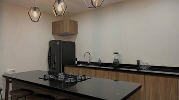 Una cocina moderna con una isla central, taburetes de bar, una estufa a gas empotrada, un refrigerador negro y lámparas colgantes hexagonales.