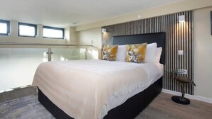A modern bedroom with a large bed, a glass railing, and a decorative wall panel. - Palm Tree House | Birds of Feather (Greater London)