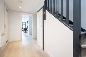 A modern interior with a staircase, a hallway leading to a dining area, and a visible kitchen. - Palm Tree House - Angles Max (Greater London)