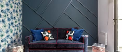 A modern living room with a dark blue accent wall, a grey sofa with red trim, and decorative pillows.