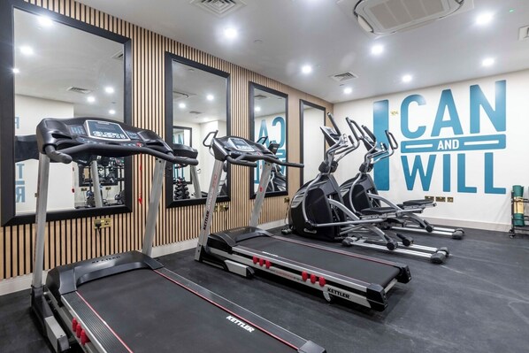 Une salle de sport équipée de tapis de course, de vélos elliptiques et d’un mur d’encouragement sur lequel on peut lire : « Je peux et je vais le faire ».