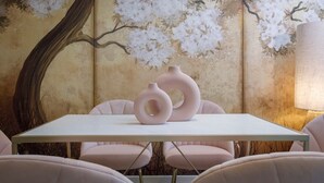 A dining area with a white table, pink chairs, and a wall mural of white flowers and a tree trunk. - Palm Tree House | Namaste (Greater London)