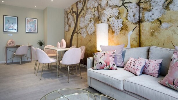 A modern living room with a large floral mural, a dining area with pink chairs, and a grey sofa with floral cushions. - Palm Tree House | Namaste (Greater London)