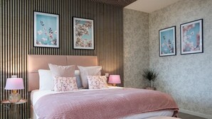 A modern bedroom with a large bed, two bedside lamps, and floral wall art. - Palm Tree House | Namaste (Greater London)