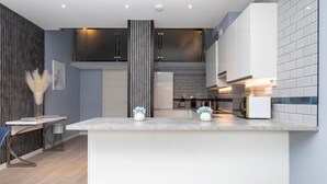 A modern kitchen with a central island, dark cabinetry, and a light-colored backsplash. - Palm Tree House - Winter Wonderland (Greater London)