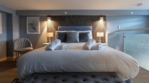 A modern hotel bedroom with a large bed, two bedside lamps, a chair, and a glass shower enclosure. - Palm Tree House - Winter Wonderland (Greater London)