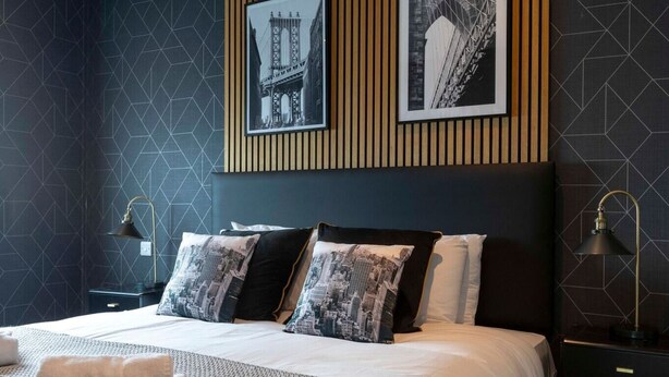 Een moderne hotelkamer met een groot bed, wanden met een geometrisch patroon en stadsfotografie op het hoofdeinde.