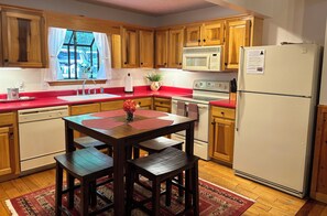 A kitchen with wooden cabinets, a red countertop, a white refrigerator, and a dining table with benches.