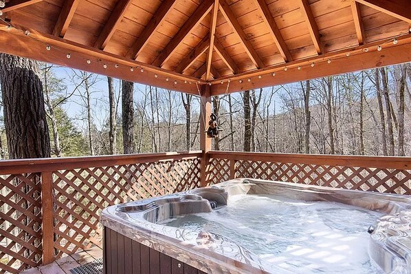 A hot tub under a wooden gazebo with a lattice railing, surrounded by trees.