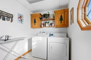 A laundry area with two white washing machines, wooden cabinets with tree designs, a drying rack, and a 'Laundry' sign.