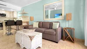 A modern living room with a grey sofa, white coffee table, and a kitchen area in the background. - Charming Condo in Prime Location @ Wacamaya Condos (Noord)