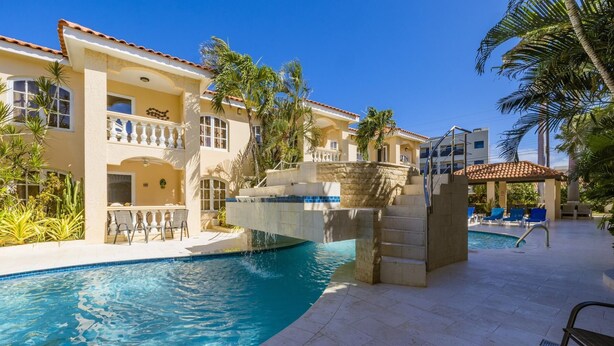 A pool area with a clear blue pool, a stone staircase, and a covered seating area with lounge chairs. - Charming Condo in Prime Location @ Wacamaya Condos (Noord)