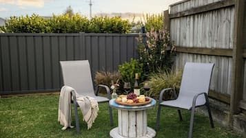 A round outdoor table with a white top and a wooden base, surrounded by two chairs with grey upholstery.
