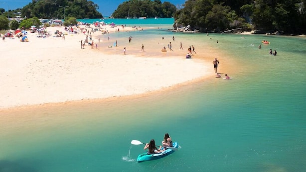 A beach with clear turquoise water, a sandy shore, and a few people kayaking. - Sun Kissed Studio  (Motueka)