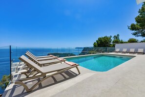 Une piscine dotée de chaises longues, offrant une vue dégagée sur l’océan et présentant un design architectural moderne.