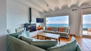 A living room with a sofa, a coffee table, a fireplace, a TV, and a large window with a view of the sea. - El Faro - By Almarina Villas (JÁVEA)