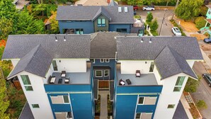 Ein modernes, zweistöckiges Wohngebäude mit einem zentralen Eingang, zahlreichen Fenstern und einer überdachten Sitzgelegenheit im Freien.