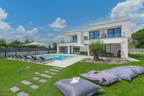Una casa moderna de dos pisos con piscina, mobiliario exterior y un césped bien cuidado.