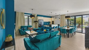A modern living area with teal sofas, a dining table, and a kitchen in the background. - 78 (Medulin)