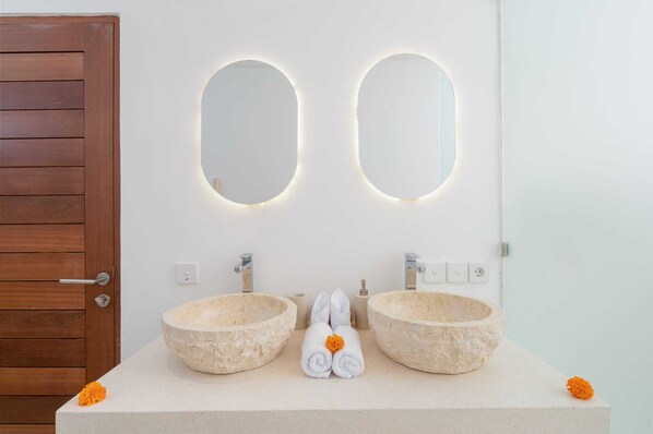 A bathroom with two stone sinks, a wooden door, and a mirror with illuminated edges. - Villa Lior (Tabanan)