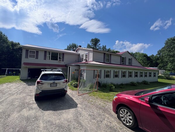 A two-story house with a garage, a red sports car, and a white SUV parked in front.