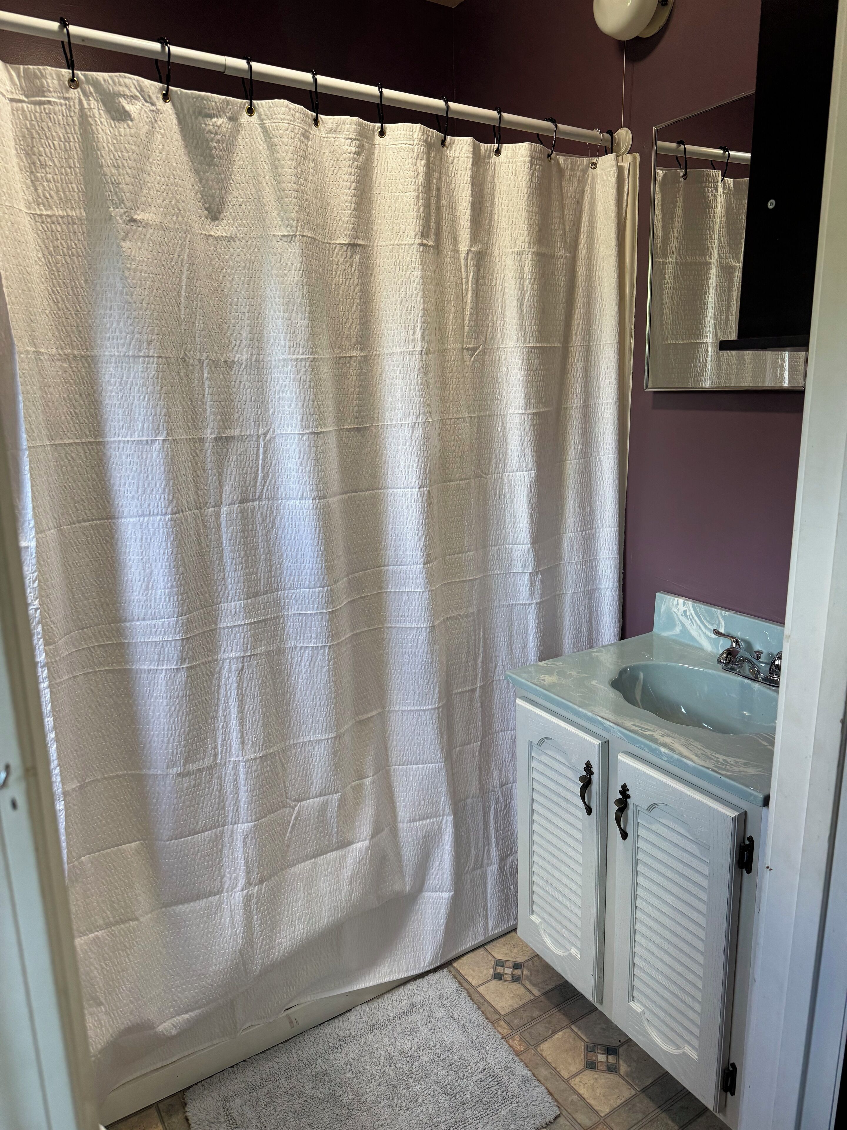 A bathroom with a white shower curtain, a sink with a marble countertop, and a mirror above the sink.