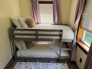 Ein Etagenbett mit zwei Schlafstellen, ein Fenster mit Jalousien und ein gemustertes Teppich.