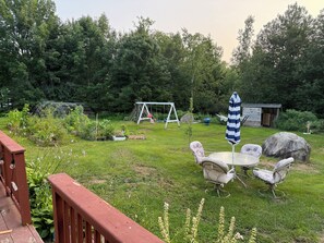 Ein Garten mit Schaukel, einer kleinen Gartenhütte und einem Tisch mit Stühlen.