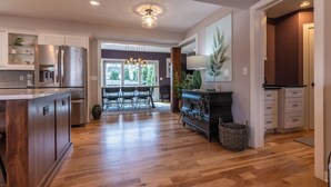A modern kitchen with a central island, wooden flooring, and a dining area with a table and chairs.
