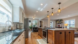 A modern kitchen with a large island, wooden cabinets, and pendant lighting.
