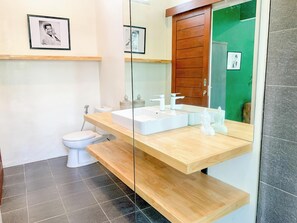 A modern bathroom with a white toilet, a large mirror, and a wooden vanity with a sink. - LANE HOUSE 1 (Canggu)