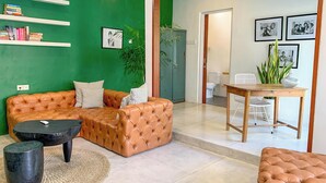 A modern living room with a brown leather sofa, a coffee table, and a dining table with chairs. There are shelves with books and framed pictures on the wall. - LANE HOUSE 1 (Canggu)