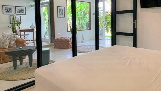 A bedroom with a large bed, a sofa, and a dining area with a table and chairs. - LANE HOUSE 1 (Canggu)