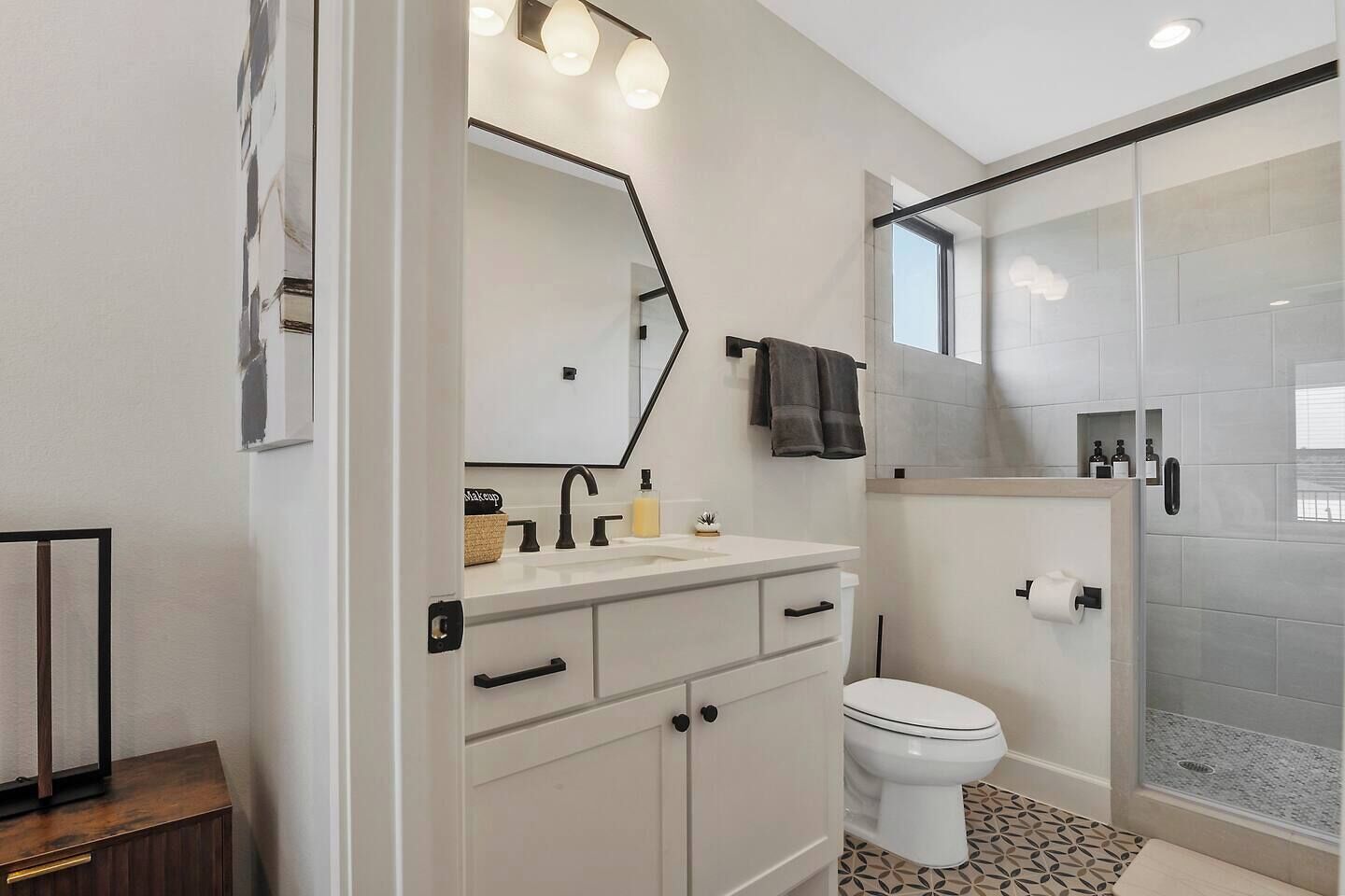 A modern bathroom with a white vanity, a large mirror, a toilet, and a glass shower enclosure.