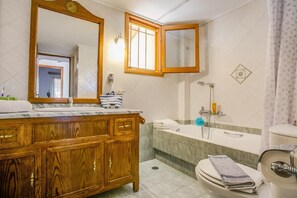 Een badkamer met een houten wastafel, een grote spiegel, een badkuip en een toilet.