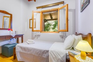 Een slaapkamer met een bed, een bureau, een stoel, een raam met gordijnen en een lamp.
