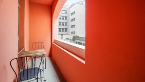 A small balcony with a view of a white building, a wooden table, and two chairs.