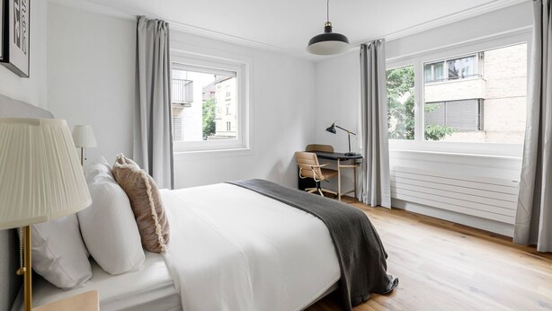 A bedroom with a bed, a desk, and two windows.