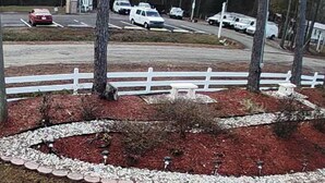 A landscaped area with a white fence, trees, and a parking lot with cars. - Cozy 4-bedroom house in welcoming Longs with WiFi, AC (Longs)