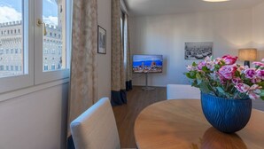 Una habitación de hotel con un ventanal grande, un televisor, una mesa de comedor con un florero y una lámpara.