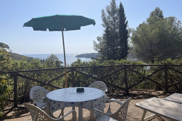 A terrace with a table and chairs, a green umbrella, and a view of the sea.