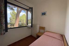 Une chambre à coucher avec un lit, une fenêtre donnant sur des arbres, une commode et une chaise.
