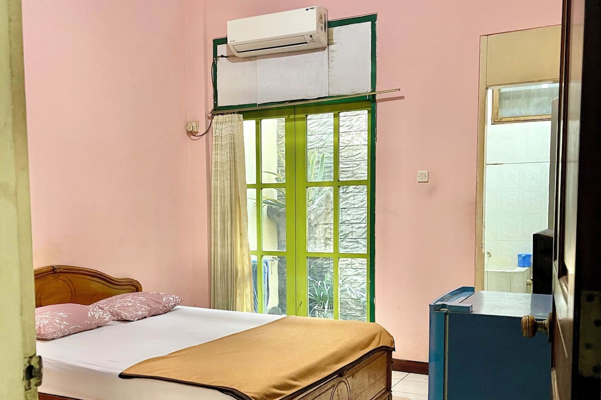 Quarto com cama, ar-condicionado, janela com cortinas e um armário azul.