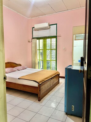 A bedroom with a bed, an air conditioner, a window with curtains, and a blue cabinet. - Hotel Tirtonadi Permai (Surakarta)