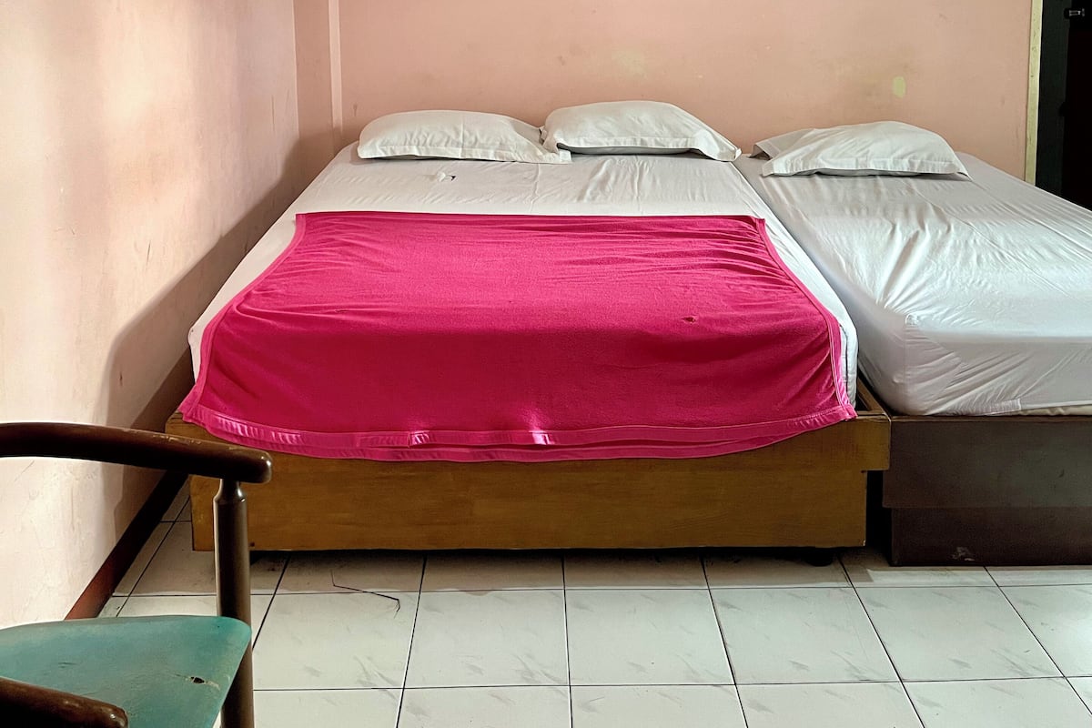 Quarto com duas camas, cabeceira de madeira, parede rosa e um quadro emoldurado.