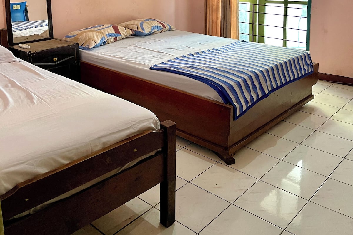 Quarto com duas camas, um espelho, uma mesinha de cabeceira, ar-condicionado e uma janela com cortinas.