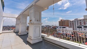 Un balcón con columnas blancas y barandilla metálica, con vista a un paisaje urbano.