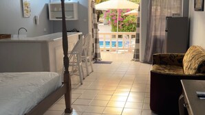 Une chambre à coucher avec un lit à baldaquin, un bureau, une chaise et une vue sur l’espace piscine.