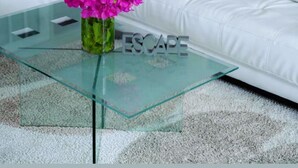 Un canapé blanc, une table basse en verre ornée d’un vase de fleurs roses, et le mot « ÉVASION » inscrit sur la table.