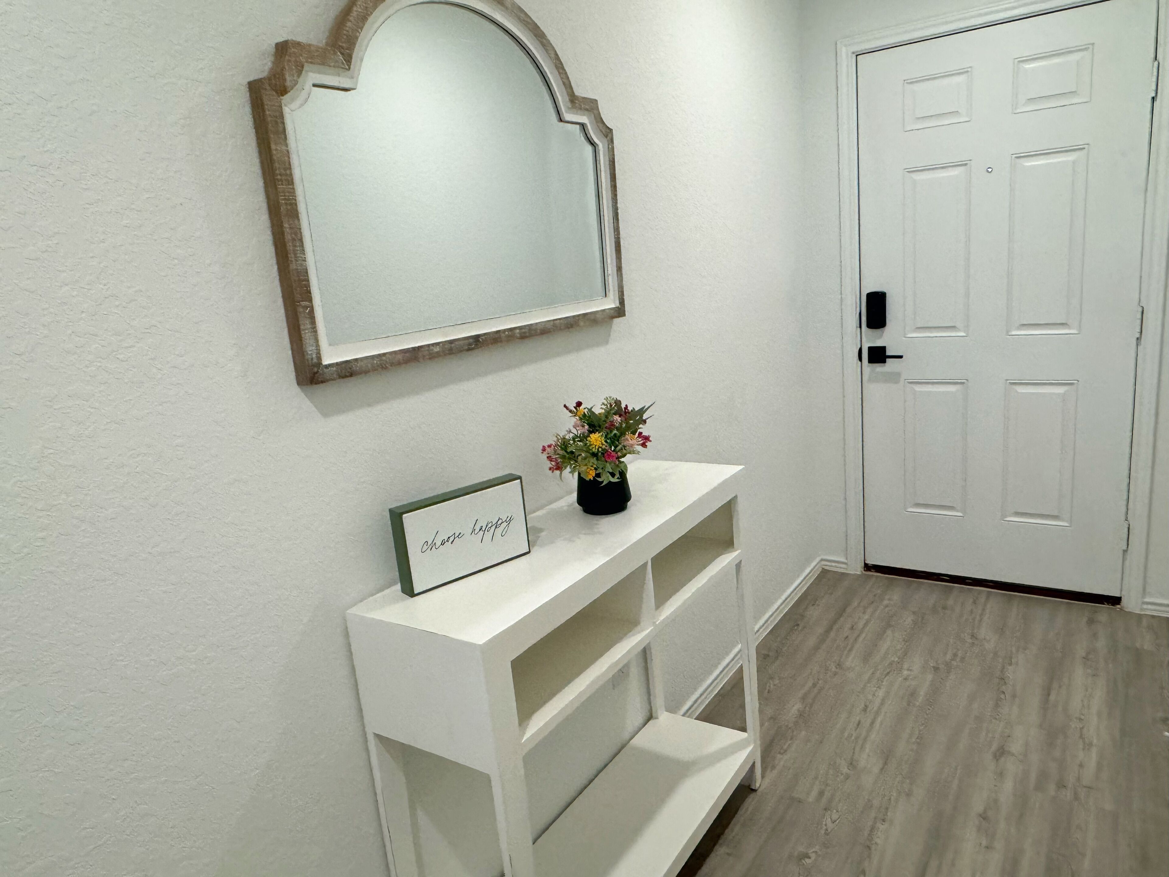A hallway with a white console table, a framed mirror, and a door.